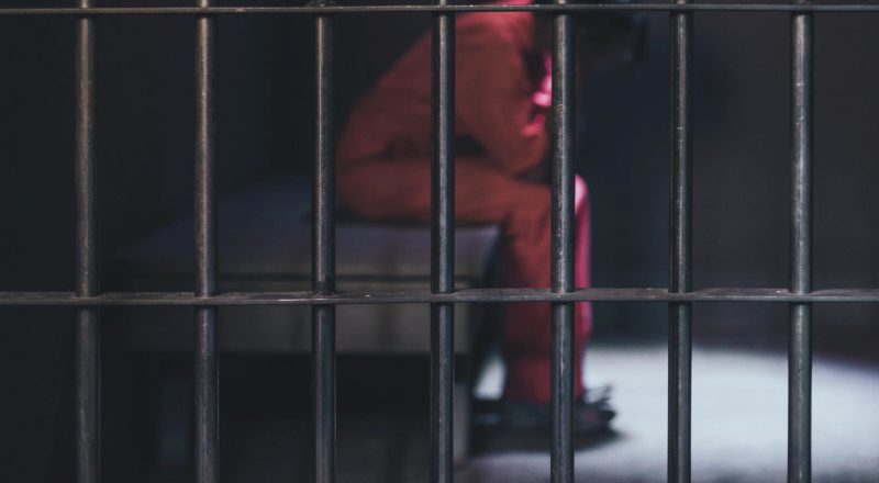 bars of a jail cell with an inmate in the blurred background